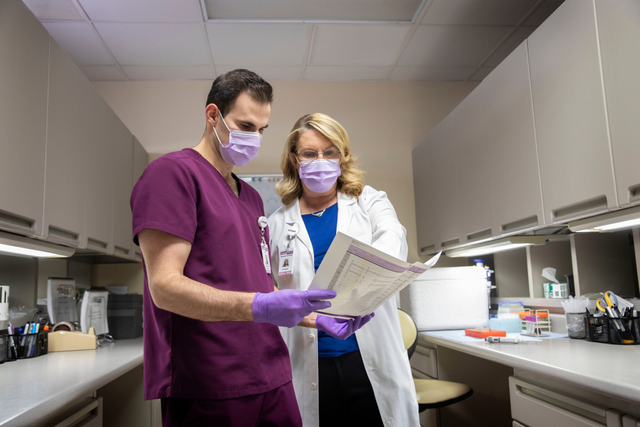 Two healthcare professionals wearing masks and gloves review a document together in a medical office.